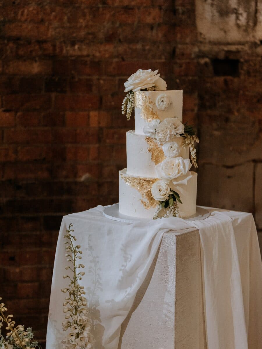 A three-tier white wedding cake dressed with roses and dried blooms